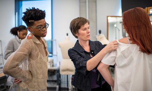 Student looks on as Professor Trippeer fits a garment to a model.