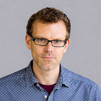 Tyson is facing forward wearing glasses. He has short brown hair and is wearing a blue shirt.