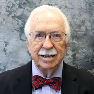 Jack Davis is facing forward and smiling. He has white hair, a white mustache and wears a blue shirt and black jacket with a bow tie,