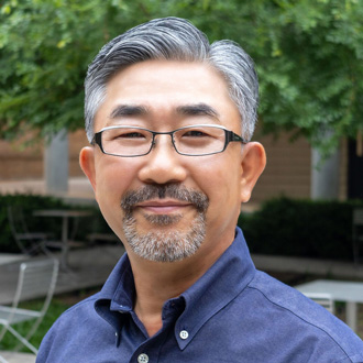 Dr. Park is facing forward and smiling. He has gray and black hair, wears glasses and a blue shirt