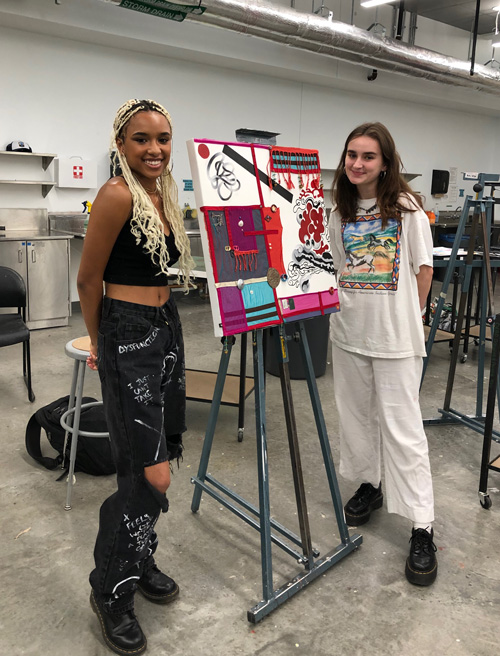 Students stand next to an easel.